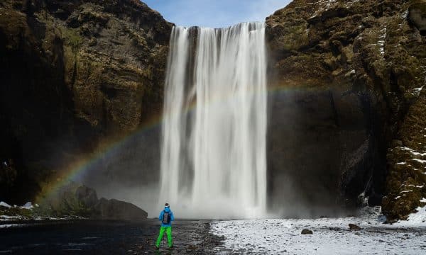 Arc-en-ciel et un homme devant la puissante cascade de Skogafoss sur la côte sud de l'Islande