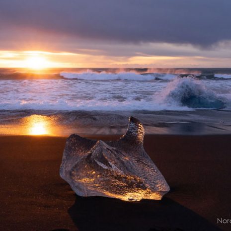 Un bloc de glace au coucher du soleil sur une plage de sable noir, communément appelée Diamond Beach