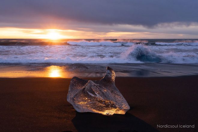 Un bloc de glace au coucher du soleil sur une plage de sable noir, communément appelée Diamond Beach