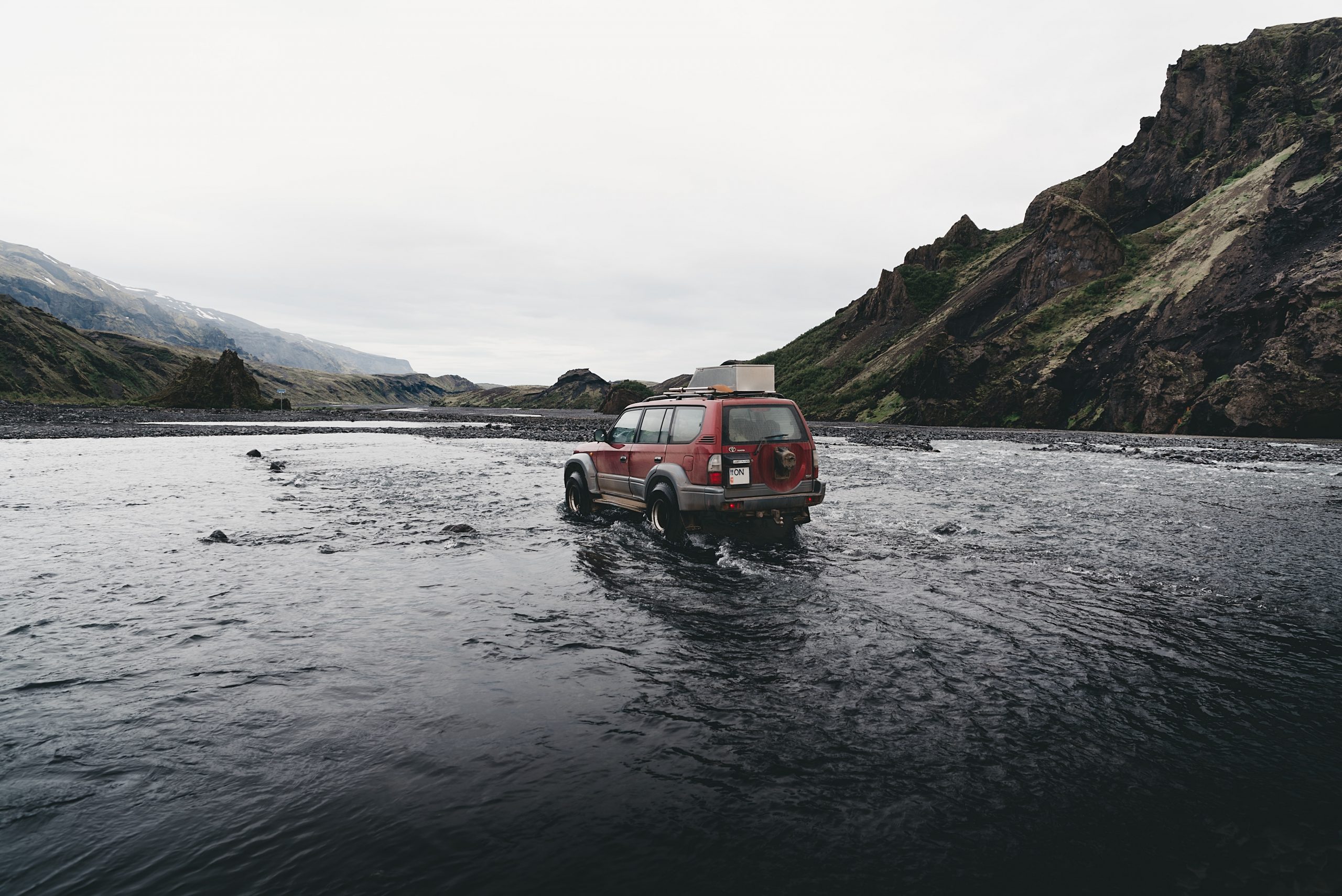 A red car crossing a river in the Icelandic Highlands.