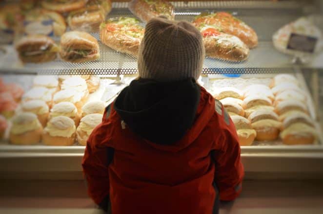 Un enfant debout devant des pâtisseries dans une vitrine.