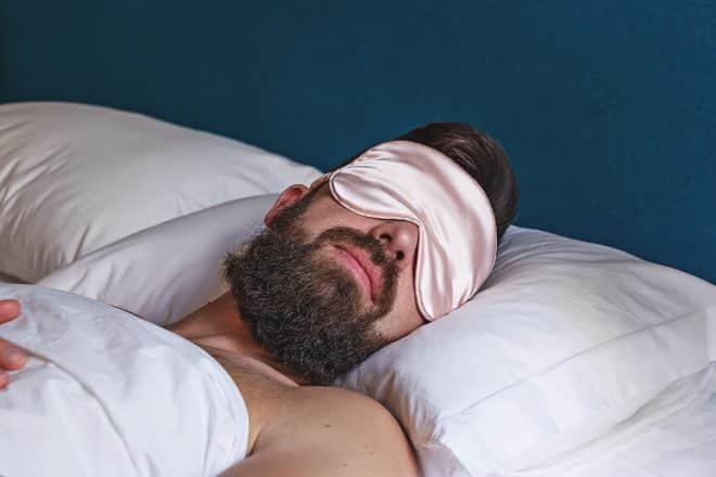 Gros plan d'un homme barbu en masque pour les yeux dormant dans son lit