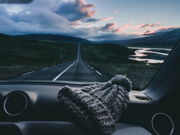 View of a road in Iceland from inside of a car with knitted hat on the dashboard.