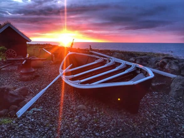 Une barque sur une plage de galets noirs au coucher du soleil en Islande