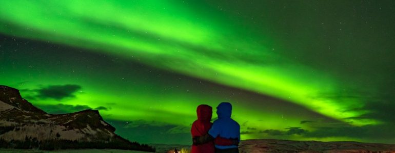 Les aurores boréales brillent sur un couple de voyageurs